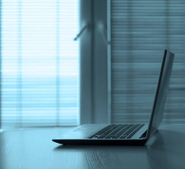 Modern bir ofiste ahşap bir masada gri bir dizüstü bilgisayar. Yazı için boş kopyalama alanı.