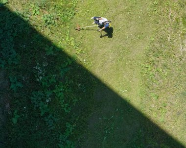 Üst görüntü. Çim biçme makinesiyle çim biçen kirli çim biçme makinesi işçisi. ışık ve gölge.