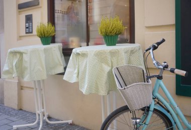 Modern bir kafenin yanında beyaz sepeti olan mavi bir bisiklet. Yeni rahat cadde. Çiçekli masalar. Salzburg, Avusturya.