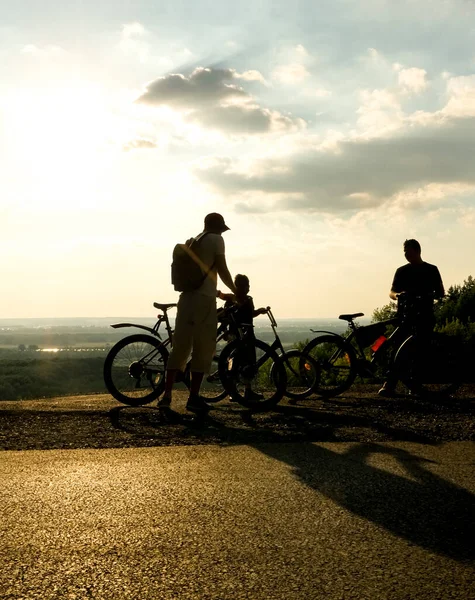 自転車のそばにリュックを持った2人の少年と父親 日当たりの良い風景 夕焼け空を背景にしたスポーツファミリーサイクリングのシルエット — ストック写真