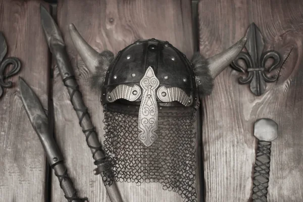 Metal medieval military helmet with horns and two srears on wooden wall background.