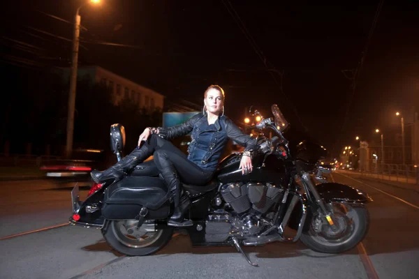 girl on motorcycle. The side of the road, the lights of the night city backgroung.Young woman sitting a motorcycle through the streets.Bike. Sexy girl. night scene.