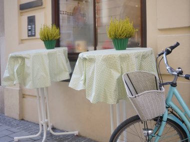 Modern bir kafenin yanında beyaz sepeti olan mavi bir bisiklet. Yeni rahat cadde. Çiçekli masalar. Salzburg, Avusturya.