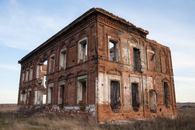 Penceresi kırık ve çatısı olmayan terk edilmiş bir bina. Tarladaki eski kırmızı tuğlalı ev. Gökyüzü zemininde birçok boş penceresi olan eski yıkılmış tuğla bina
