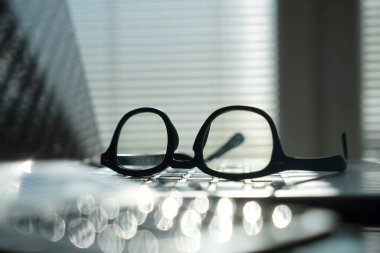 Dizüstü bilgisayarı ve gözlüklü bir ofis. Bilgisayarlı pencerelerin yanındaki ofis masasının görüntüsü. İş ya da iş kavramı.