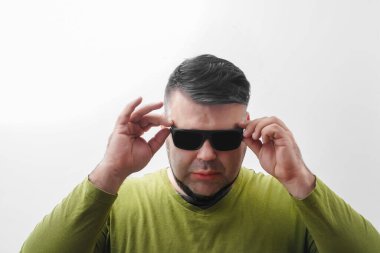 Yeşil tişörtlü ve güneş gözlüklü genç seksi adam aşağıya bakıyor. Beyaz arka planda izole edilmiş. Genç bir erkek. Sakallı hippi eşcinsel