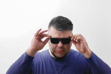 Yeşil tişörtlü ve güneş gözlüklü genç seksi adam aşağıya bakıyor. Beyaz arka planda izole edilmiş. Genç bir erkek. Sakallı hippi eşcinsel