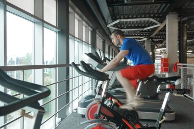 Spor salonunda bisiklet kullanan kaslı bir adam. Spor salonunda bisiklet kardiyo çalışması. yan görünüm.
