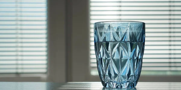 在盲窗的背景下 摆在桌子上的一面蓝色的水杯 — 图库照片