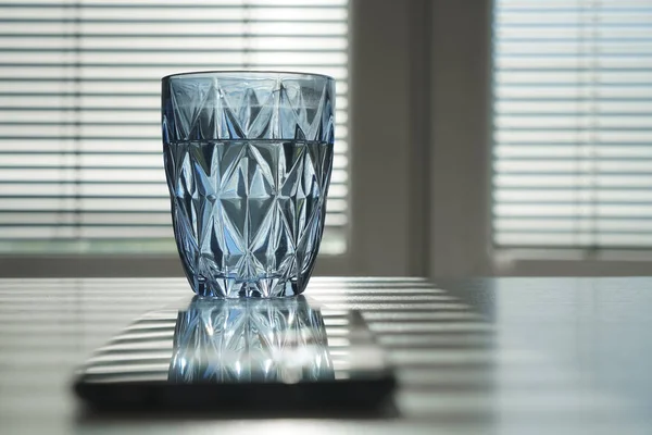 mobile phone and glass of water on blue transparent glass. reflection on screen. workplace in office room. empty copy space for inscription.