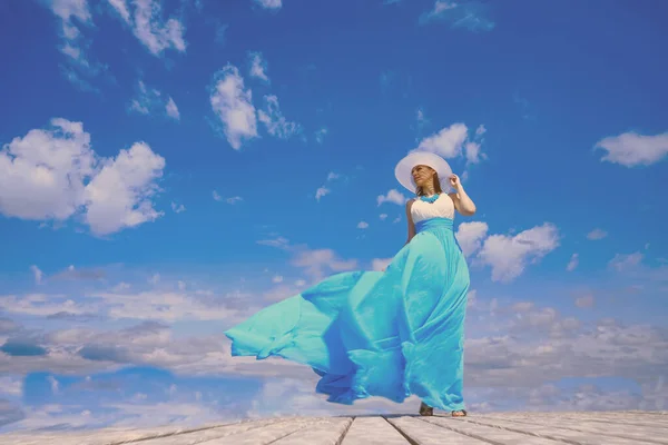 白と青のドレスの少女は木製の桟橋に立っている 青空を背景に 風の強い天気 顔の光と影 — ストック写真