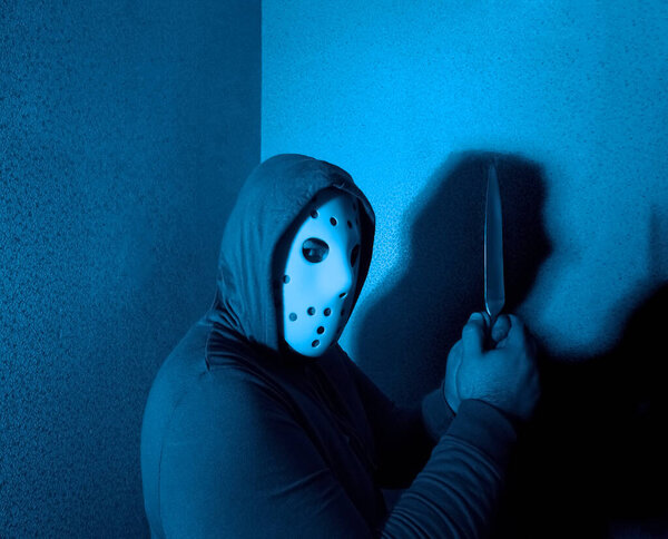 man attack with knife. The guy with the knife in hand wearing a black hood. The threat of a cold weapon. The concept of crime and robbery. neon light on background.