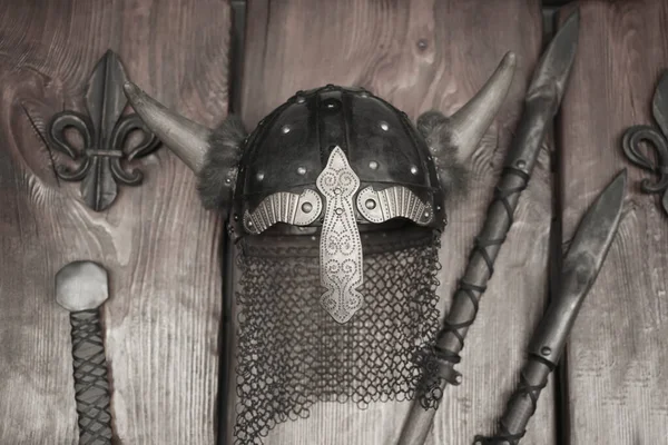 Metal medieval military helmet with horns and two srears on wooden wall background.