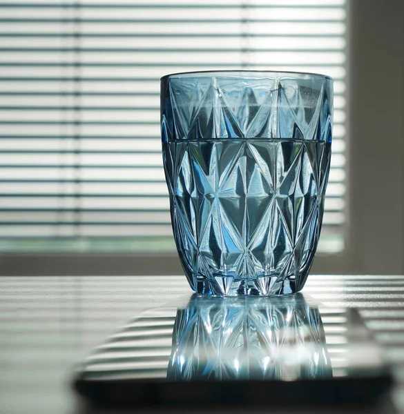 mobile phone and glass of water on blue transparent glass. reflection on screen. workplace in office room. empty copy space for inscription.