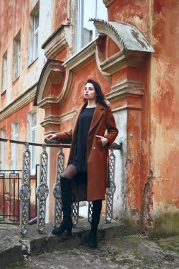 Esmer, uzun kıvırcık saçlı, haki paltolu güzel bir kız antika, eski, kırmızı tarihi bir evin arka planında duruyor. konsept tasarımı Latin Latin kadının üstündeki pencere. Sonbahar, sonbahar mevsimi 