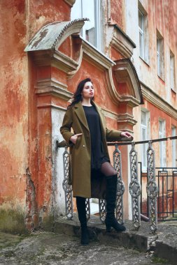 Esmer, uzun kıvırcık saçlı, haki paltolu güzel bir kız antika, eski, kırmızı tarihi bir evin arka planında duruyor. konsept tasarımı Latin Latin kadının üstündeki pencere. Sonbahar, sonbahar mevsimi 