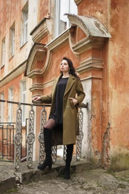 Esmer, uzun kıvırcık saçlı, haki paltolu güzel bir kız antika, eski, kırmızı tarihi bir evin arka planında duruyor. konsept tasarımı Latin Latin kadının üstündeki pencere. Sonbahar, sonbahar mevsimi 