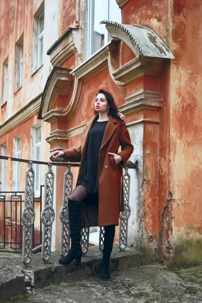 Esmer, uzun kıvırcık saçlı, haki paltolu güzel bir kız antika, eski, kırmızı tarihi bir evin arka planında duruyor. konsept tasarımı Latin Latin kadının üstündeki pencere. Sonbahar, sonbahar mevsimi 