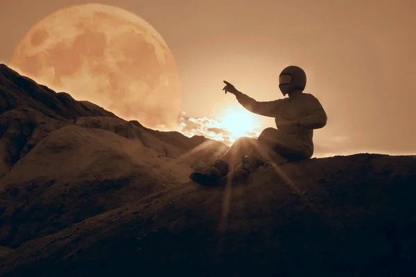 spaceman pointing at beautiful sky with stars while sitting on top of mountain. Mission specialist astronaut wearing white space suit with helmet. Concept of space travel and night sky. Side view