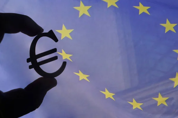 male hand hold the Euro icon silhouette on euro union flag background. sun rays. euro sign, symbol of money, idea of Euro Union