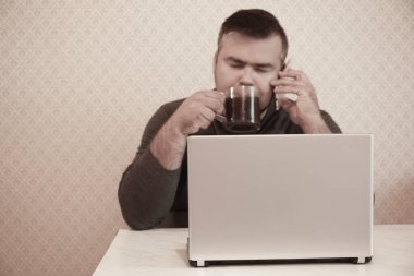 Bilgisayarlı bir iş adamı ofiste uyuyor, siyah bir kafe içiyor ve cep telefonuyla konuşuyor. Kapalı gözlü erkek..