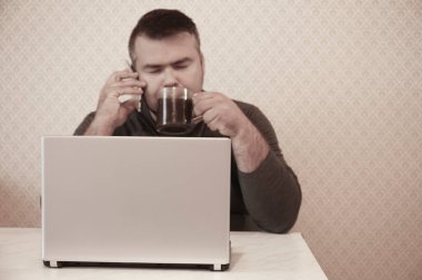 Bilgisayarlı bir iş adamı ofiste uyuyor, siyah bir kafe içiyor ve cep telefonuyla konuşuyor. Kapalı gözlü erkek..