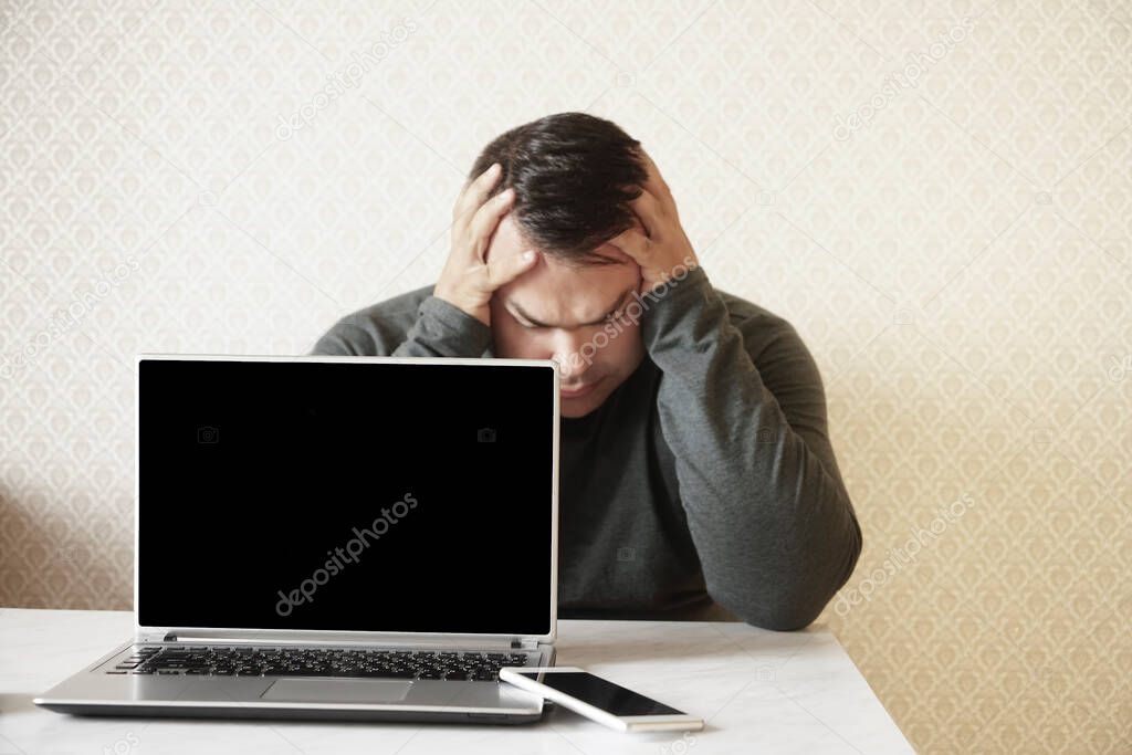 Young upset businessman is working in modern light office under stress. Feel of tiredness. A man sits at a table indoors with a laptop and eyes closed tiredness drowsiness