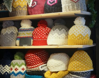 Mağaza raflarında renkli örgü şapkalar satışı. Fiyat işaretli ponponlu çok renkli şapkalarla dolu raflar.