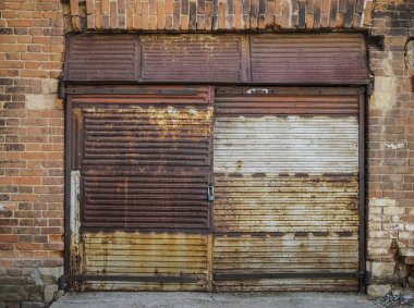 Eski bir garajın ön cephesi kırmızı tuğladan yapılmış büyük paslı kapılı yeşil çimlerde. Ön manzara. asma kilit