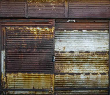 Eski bir garajın ön cephesi kırmızı tuğladan yapılmış büyük paslı kapılı yeşil çimlerde. Ön manzara. asma kilit