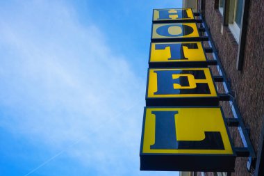 Mavi gökyüzüne karşı binanın köşesinde neon otel tabelası. Yazı için boş kopyalama alanı. Modern sarı işaret. Dikey otel işareti. Amsterdam, Hollanda 