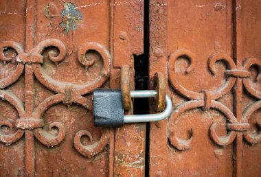 Kapalı eski metal kapılar ya da paslı asma kilitle dövülmüş kapılar. Yakından eski püskü, pörsümüş demir dokusu ve kırmızı pas lekeleri olan kahverengi boya tabakası. Arkaplan.