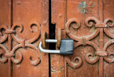Kapalı eski metal kapılar ya da paslı asma kilitle dövülmüş kapılar. Yakından eski püskü, pörsümüş demir dokusu ve kırmızı pas lekeleri olan kahverengi boya tabakası. Arkaplan.