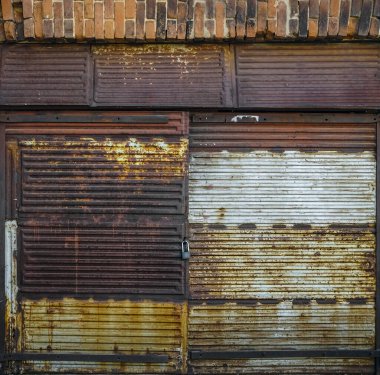 Eski bir garajın ön cephesi kırmızı tuğladan yapılmış büyük paslı kapılı yeşil çimlerde. Ön manzara. asma kilit