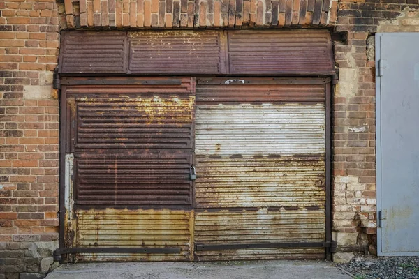 Eski bir garajın ön cephesi kırmızı tuğladan yapılmış büyük paslı kapılı yeşil çimlerde. ön görünüm.