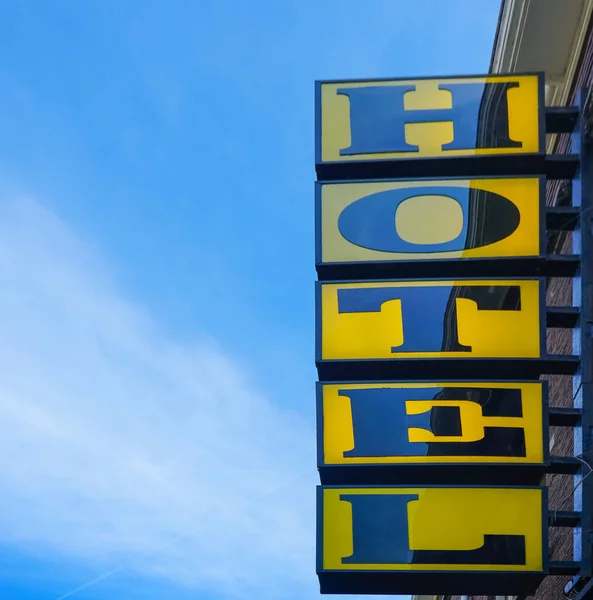 Neon hotel sign on the building corner against blue sky.  Empty copy space for inscription. modern yellow sign. Vertical hotel sign. Amsterdam, Netherlands
