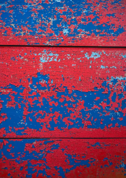 kırmızı, mavi soyulmuş boya dokusu. Çatlak boya tabakalarıyla kaplı ahşap bir yüzey.