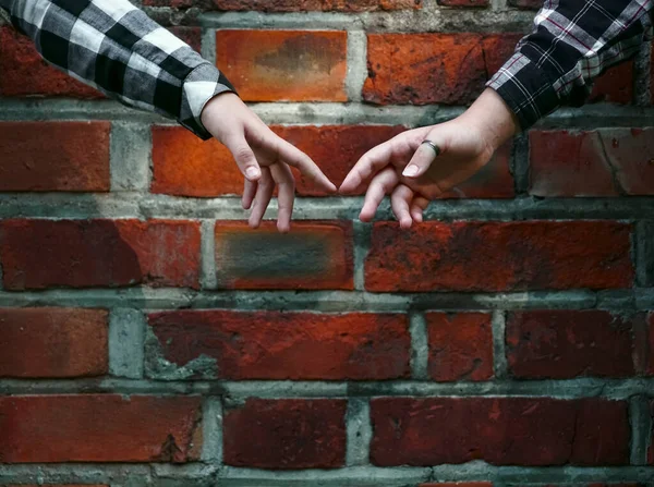 Two hands reach out to each other. The background is a red brick wall. Fragment of the painting. lesbian couple