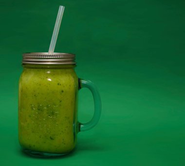 Dolu cam kavanoz, kapaklı kupa, yeşil arka planda izole edilmiş saman sapı. smoothie 