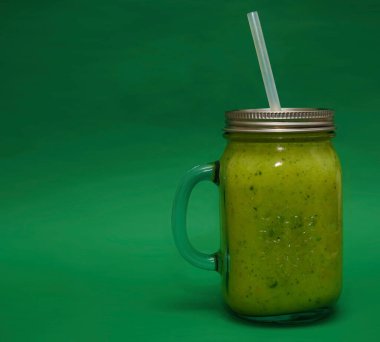 Dolu cam kavanoz, kapaklı kupa, yeşil arka planda izole edilmiş saman sapı. smoothie 