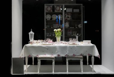 Güzel dekore edilmiş masa, beyaz tabaklar, kristal bardaklar, keten peçeteler, çatal bıçak takımı ve lüks masa örtüsü üzerinde lale çiçekleri. Dükkan penceresi. gece sahnesi