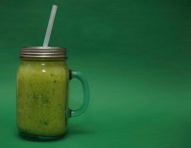 Dolu cam kavanoz, kapaklı kupa, yeşil arka planda izole edilmiş saman sapı. smoothie 
