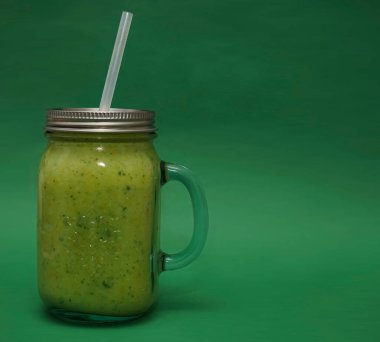 Dolu cam kavanoz, kapaklı kupa, yeşil arka planda izole edilmiş saman sapı. smoothie 