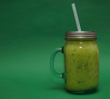 Dolu cam kavanoz, kapaklı kupa, yeşil arka planda izole edilmiş saman sapı. smoothie 