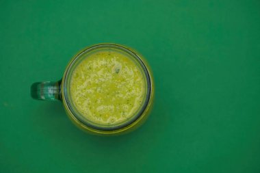 Dolu cam kavanoz, yeşil arka planda izole edilmiş kulplu bardak. Yazı için smoothie boş kopya alanı. en üstteki görünüm