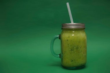 Dolu cam kavanoz, kapaklı kupa, yeşil arka planda izole edilmiş saman sapı. smoothie 