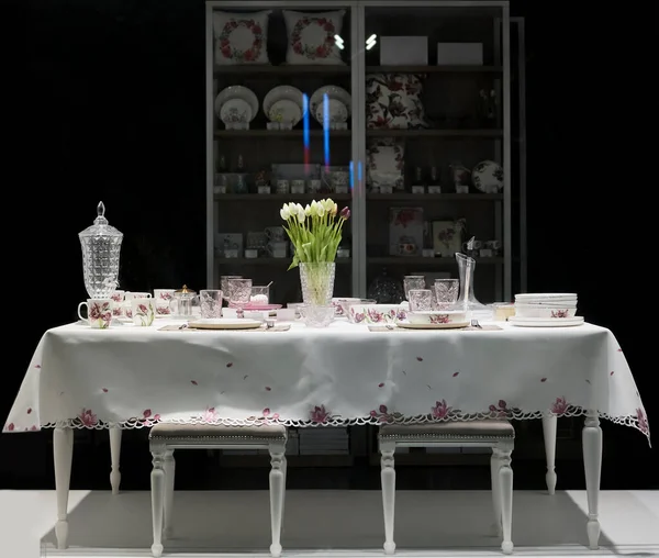 table with white plates, crystal glasses, linen napkins, cutlery and tulip flowers on luxurious tablecloth. shop window. night scene