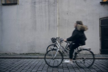 Şehir caddesinde eski bir binanın önünde bisiklet süren bulanık bir genç kadın. Amsterdam, Hollanda. Tanımlanamayan kadın 
