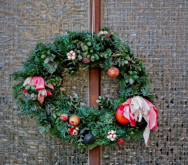christmas wreath at a glasses door. A traditional handmade Christmas wreath made of spruce and ornaments hangs on the front door of a shop or home. The concept of preparing for the New Year.