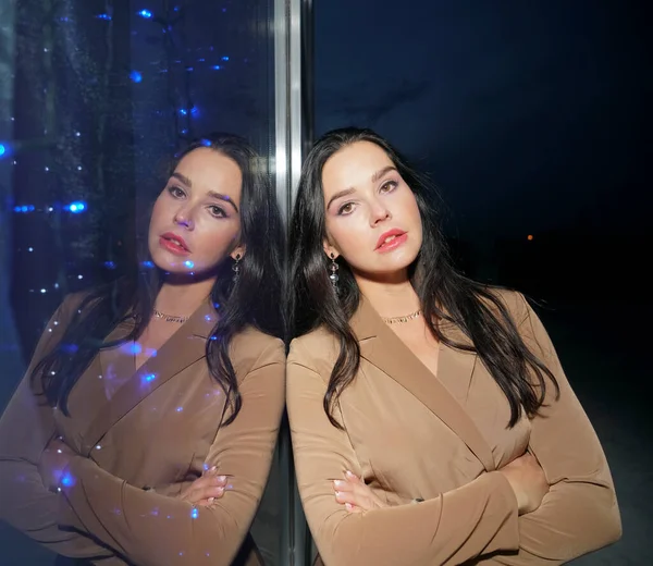 Latin asıllı genç bir kadının portresi büyük bir dükkan penceresinin yanında duruyor. Gece sahnesi. Lüks kostüm giyen esmer Asyalı kadın. Akşam ışığı. Vitrindeki yansıma. Rüya gibi bir yüz